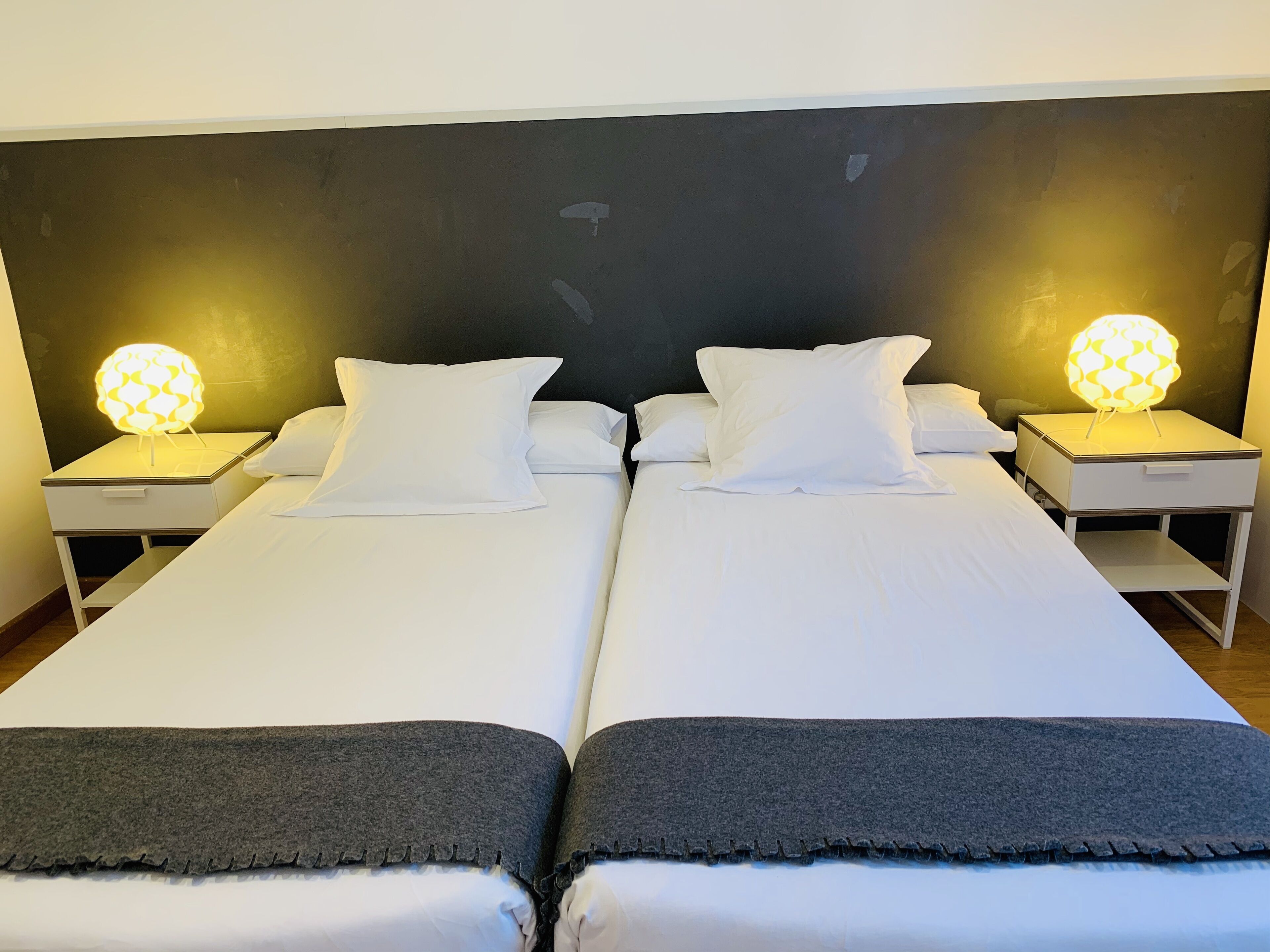 Een tweepersoonsbed met witte lakens en twee bedlampjes.