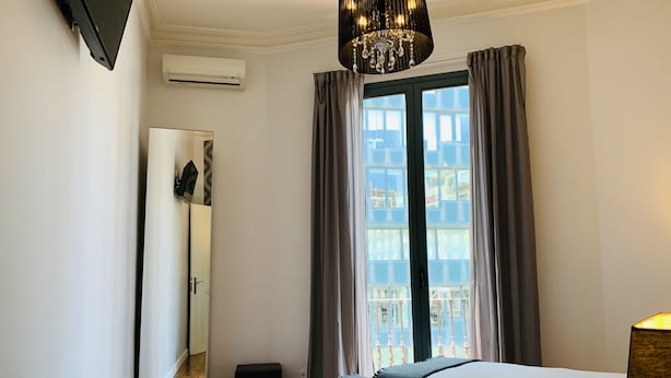 Una habitación de hotel con cama, espejo, ventana con cortinas y aire acondicionado.