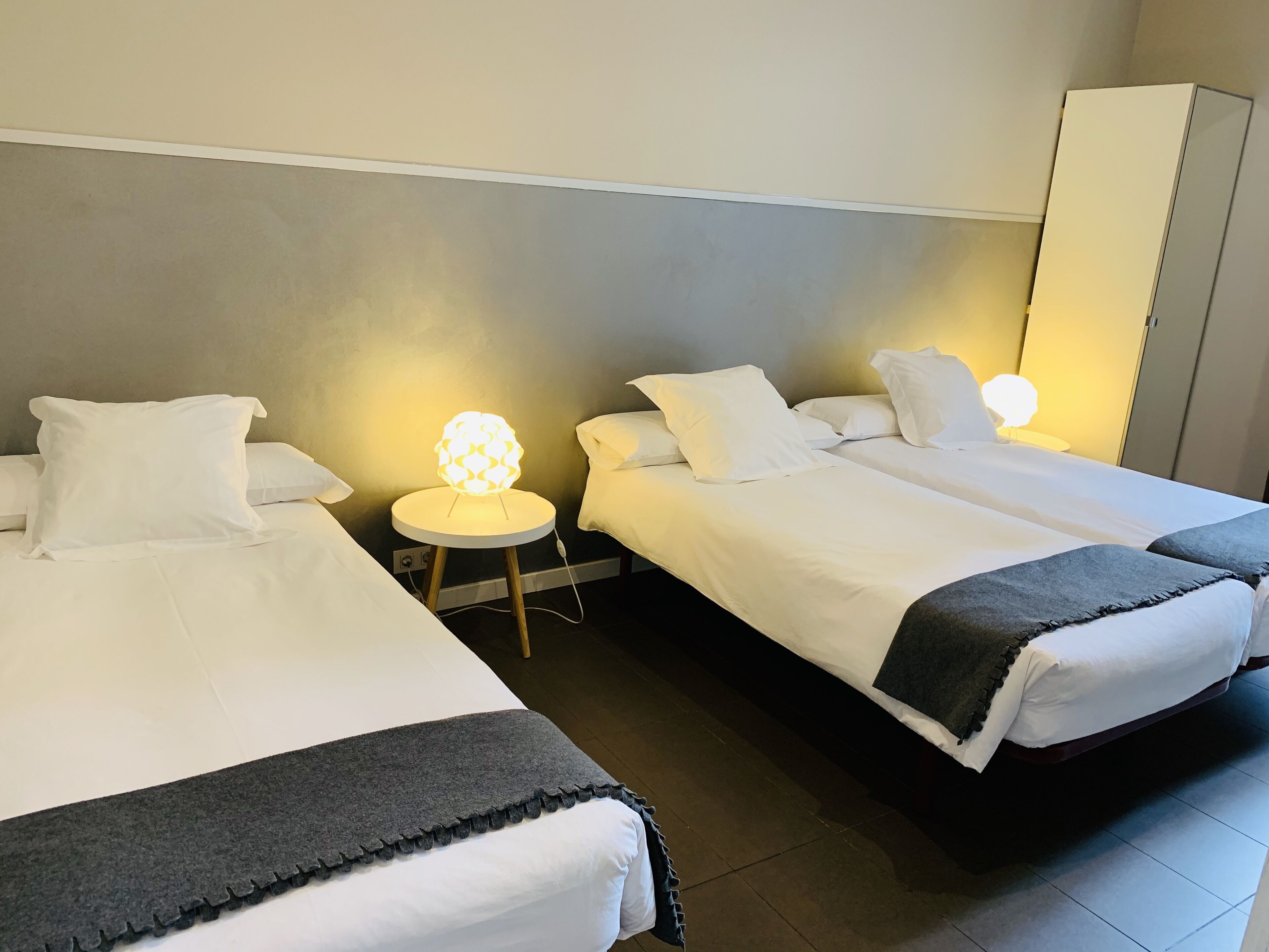 A hotel room with two single beds, a small bedside table with a lamp, and a wardrobe.