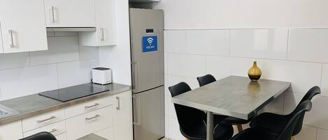 A modern kitchen with white cabinets, a stainless steel refrigerator, a toaster, and a table with four black chairs.