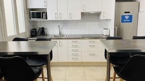 Cocina moderna con armarios blancos, pileta de acero inoxidable y microondas. Hay un cartel que indica WiFi gratuito.