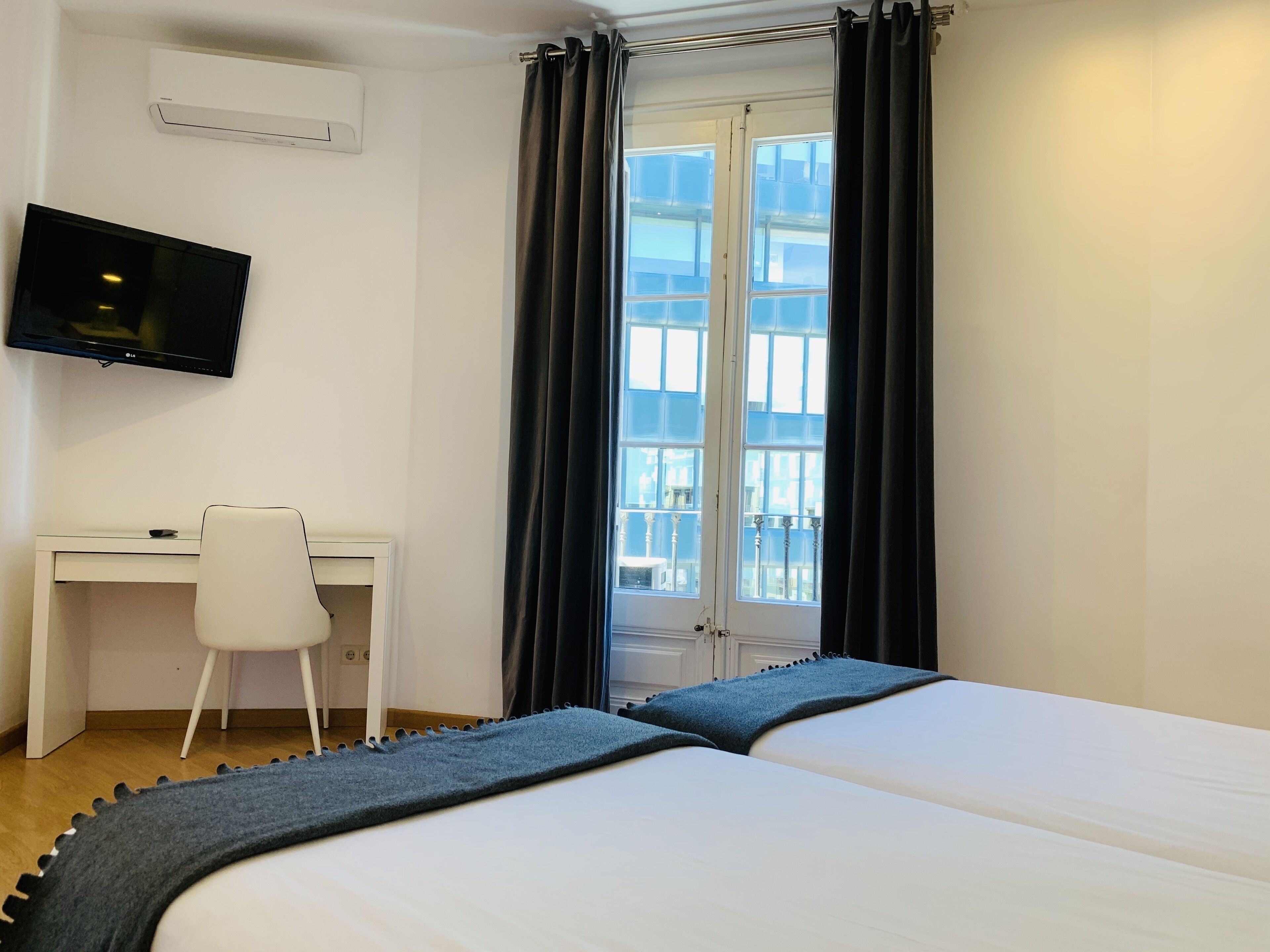 A hotel room with a bed, a desk, a chair, a TV, and a window with curtains.