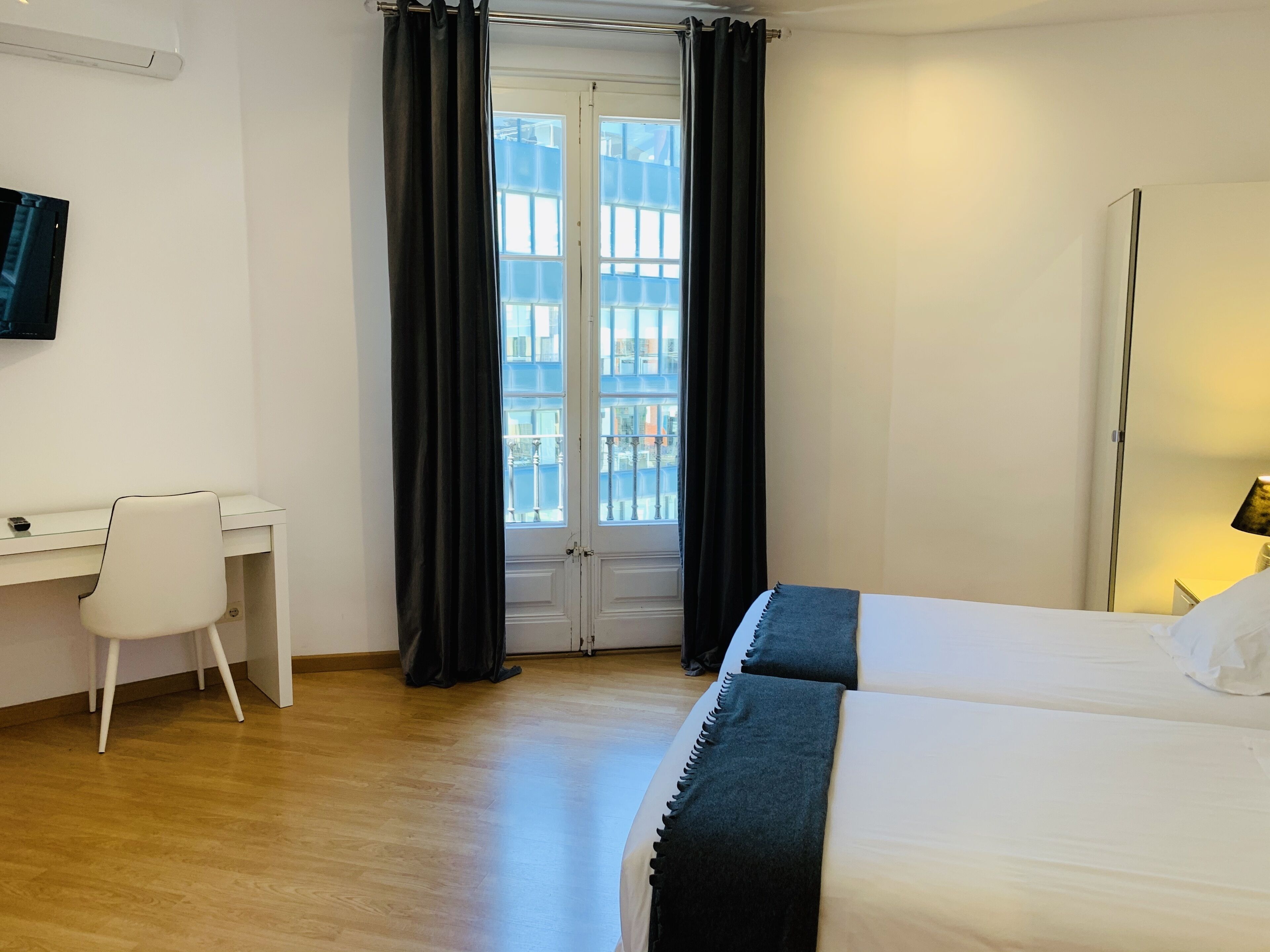 Una camera d'albergo con un letto, una scrivania, una sedia, una finestra con tende e una lampada.