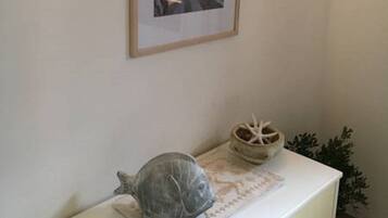 Un tableau encadré représentant une scène de rue, accroché au mur, une petite table sur laquelle se trouvent un bol décoratif et une figurine, et un meuble avec un tiroir.