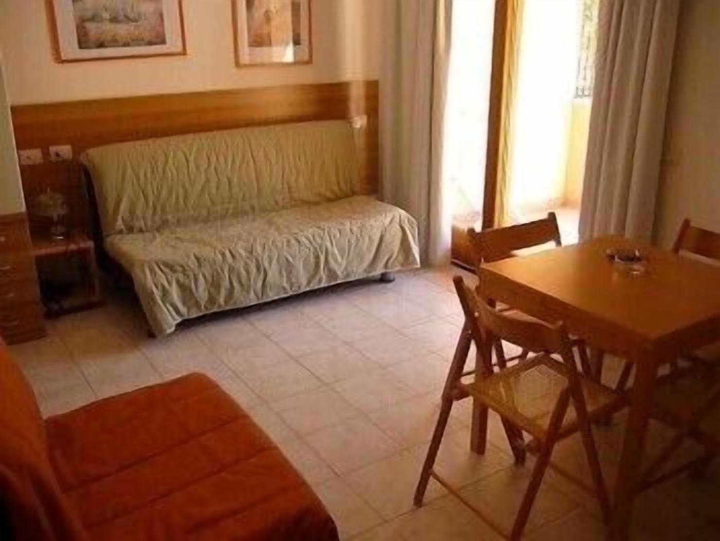 A room with a bed, a dining table with chairs, and a small table with a lamp.
