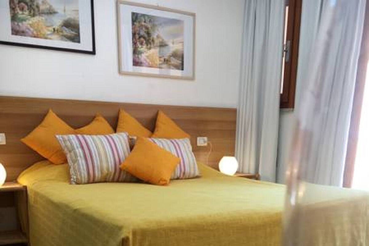 A hotel room with a bed, a nightstand, and two framed pictures on the wall.