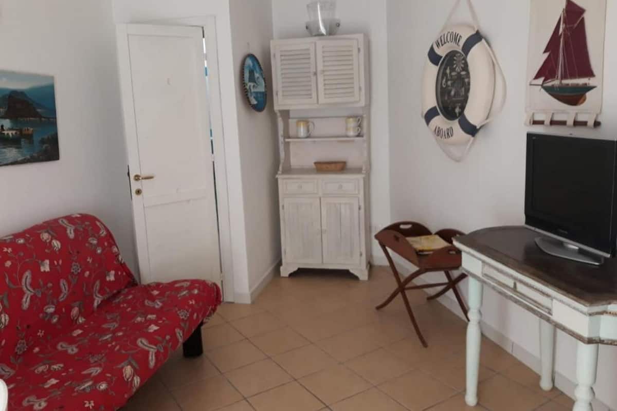 A room with a red patterned sofa, a television on a wooden table, a white cabinet, and a door.
