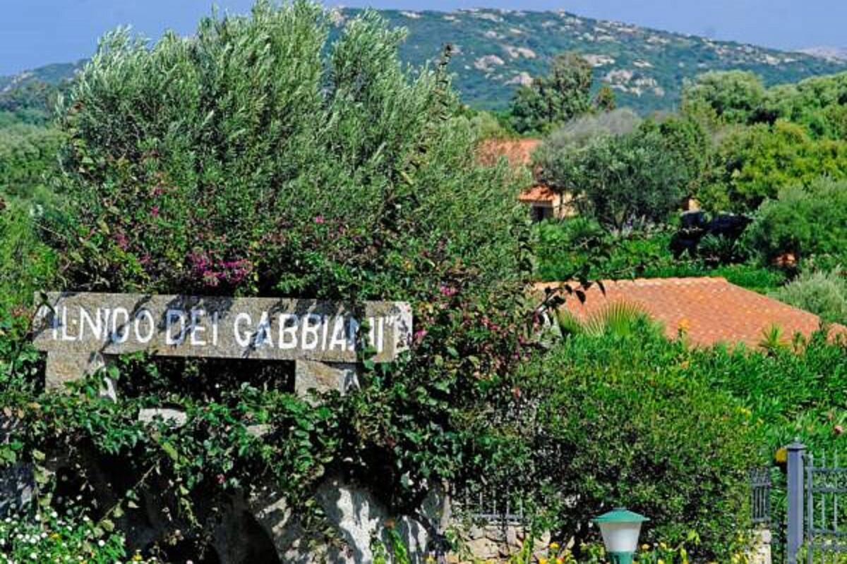 A stone sign with the text "ILNO DEI GABBIAI" surrounded by lush greenery and a mountainous backdrop.