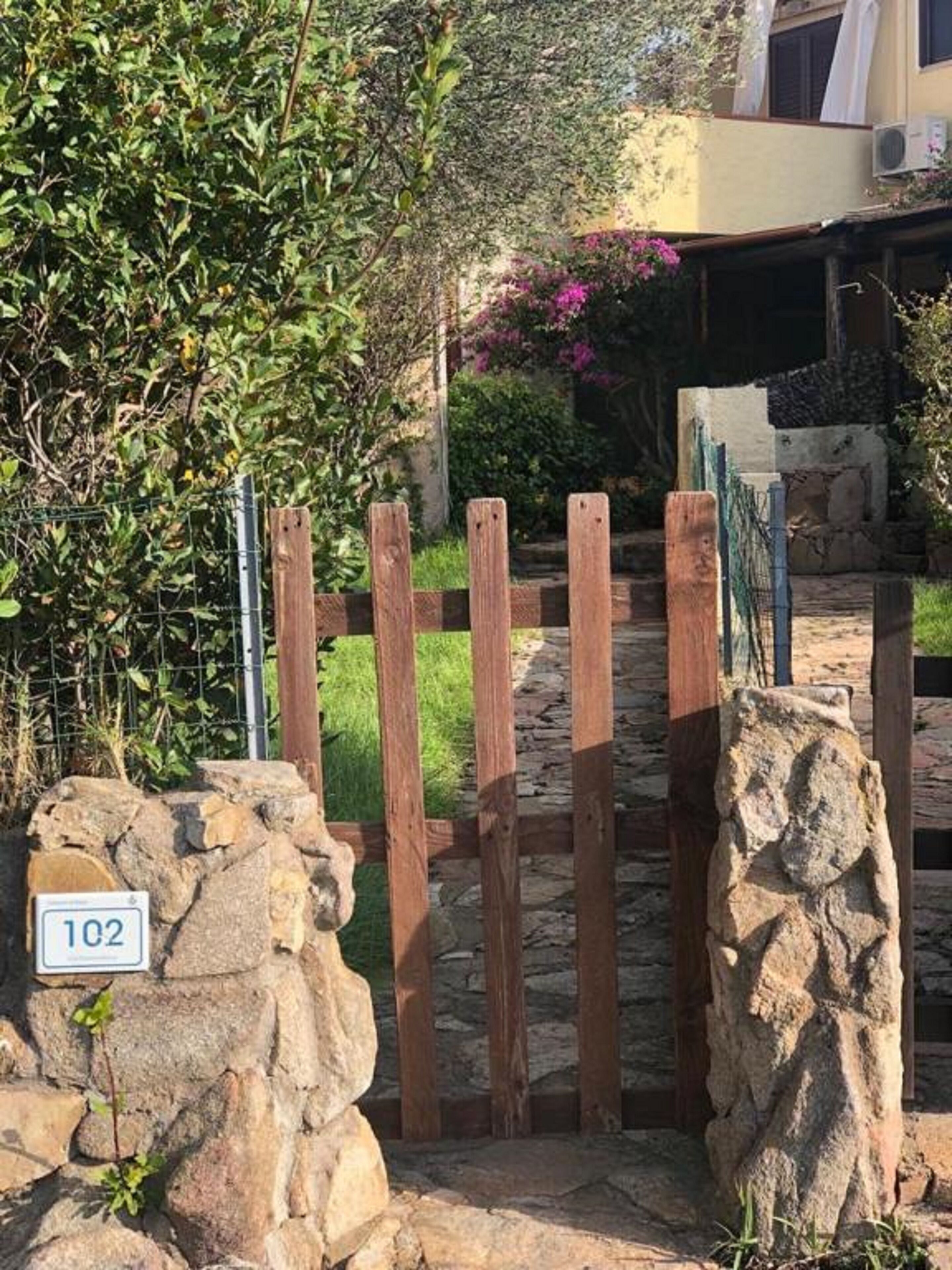 A stone pathway leading to a wooden gate, with a stone number plaque '102' visible.
