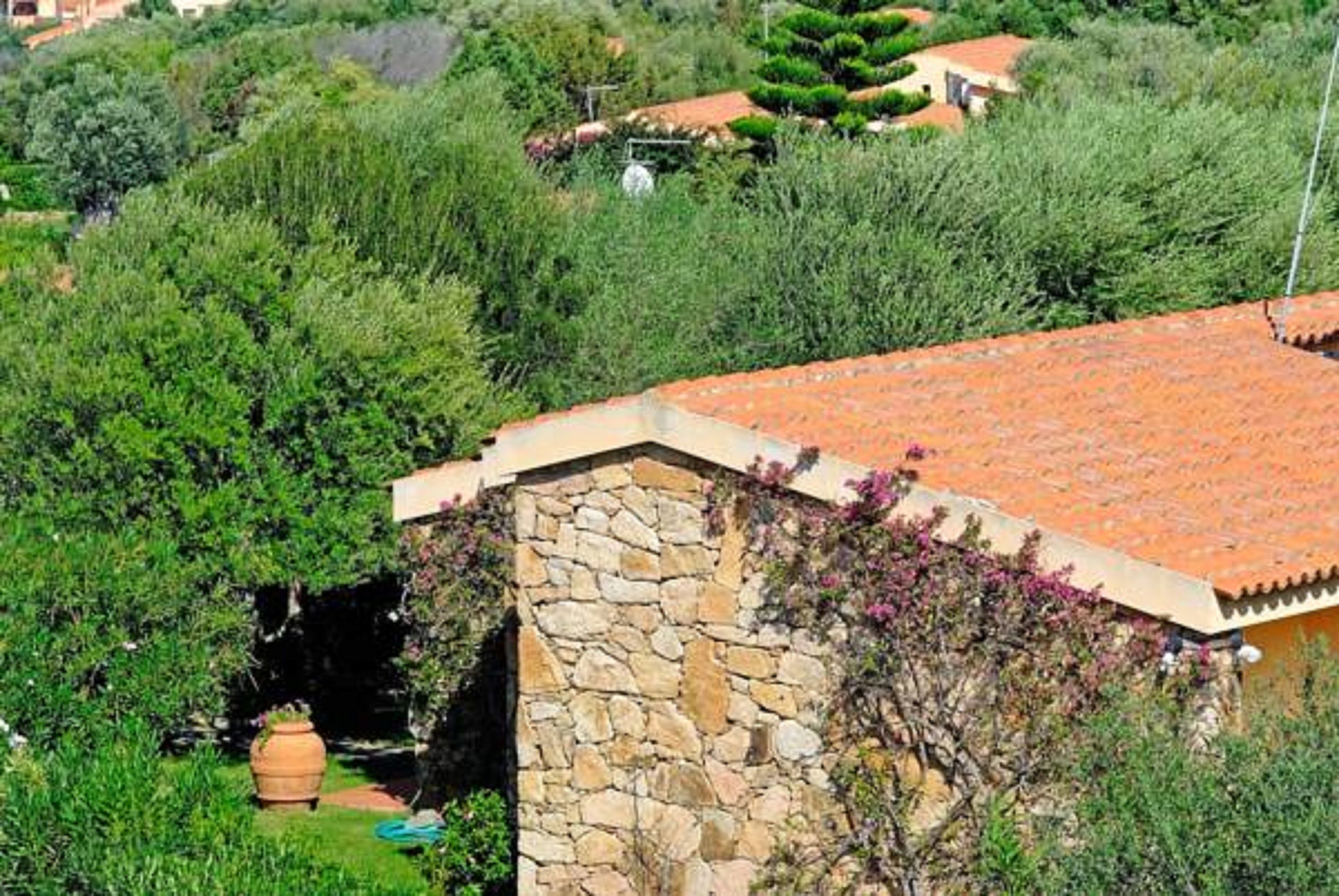 Un edificio de piedra con techo de tejas, rodeado de abundante vegetación y un jardín bien cuidado.