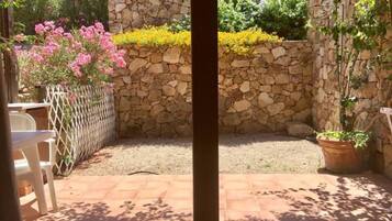 Jardín con muro de piedra, plantas en macetas y una silla blanca.