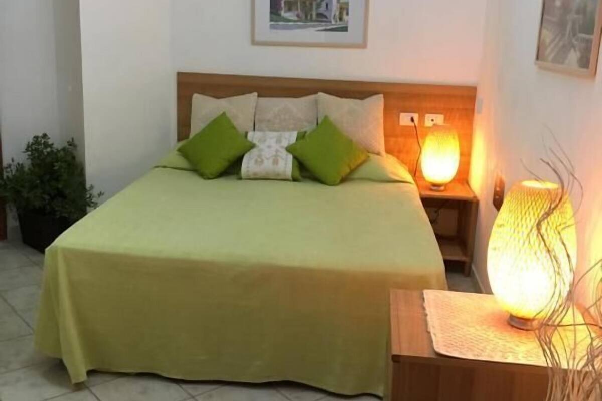 A neatly made bed with green and white bedding, a bedside lamp, and a framed picture on the wall.