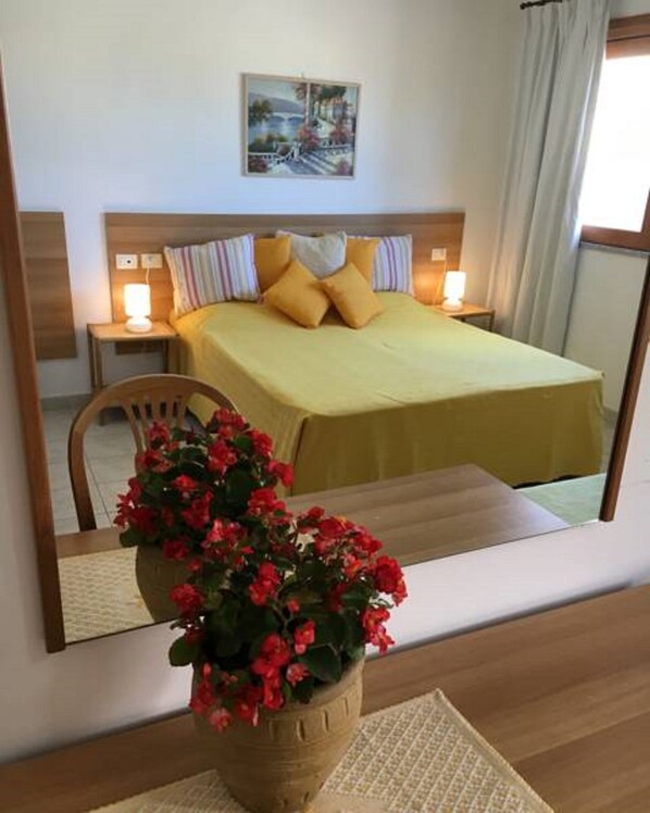 A hotel room with a bed, bedside lamps, a painting on the wall, and a potted plant with red flowers.