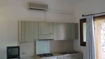Une cuisine de taille réduite équipée d’une cuisinière à gaz, d’un petit réfrigérateur, d’un téléviseur et d’un ventilateur de plafond.