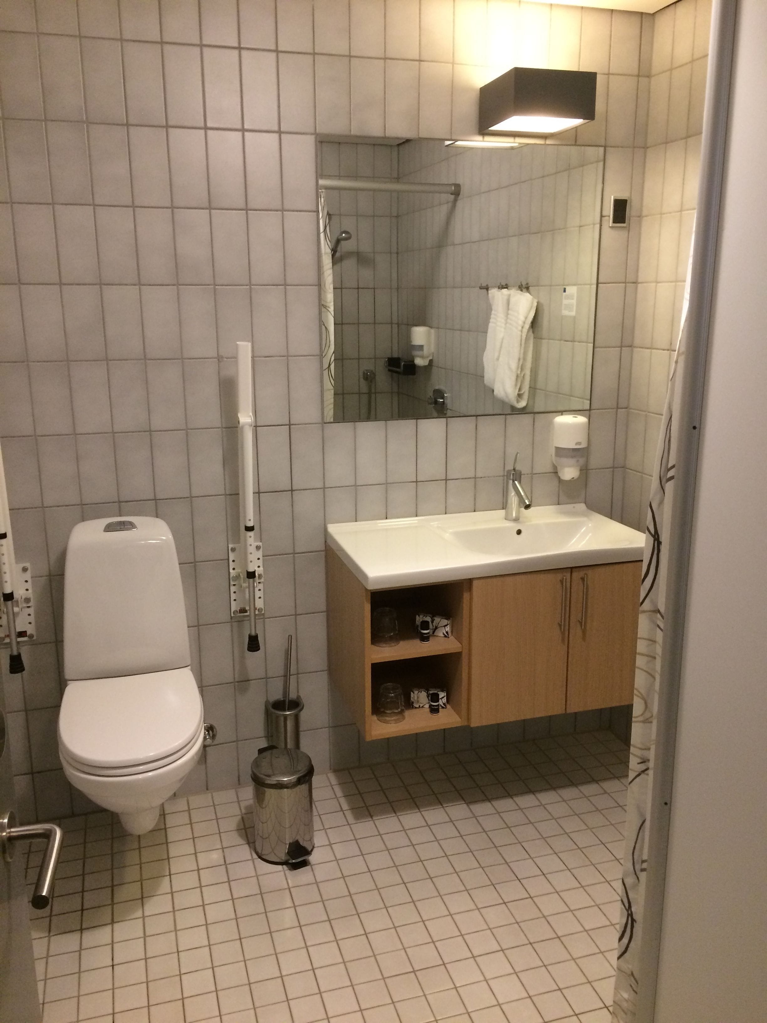 Une salle de bain comprenant des toilettes, un lavabo, un miroir et un sol carrelé.