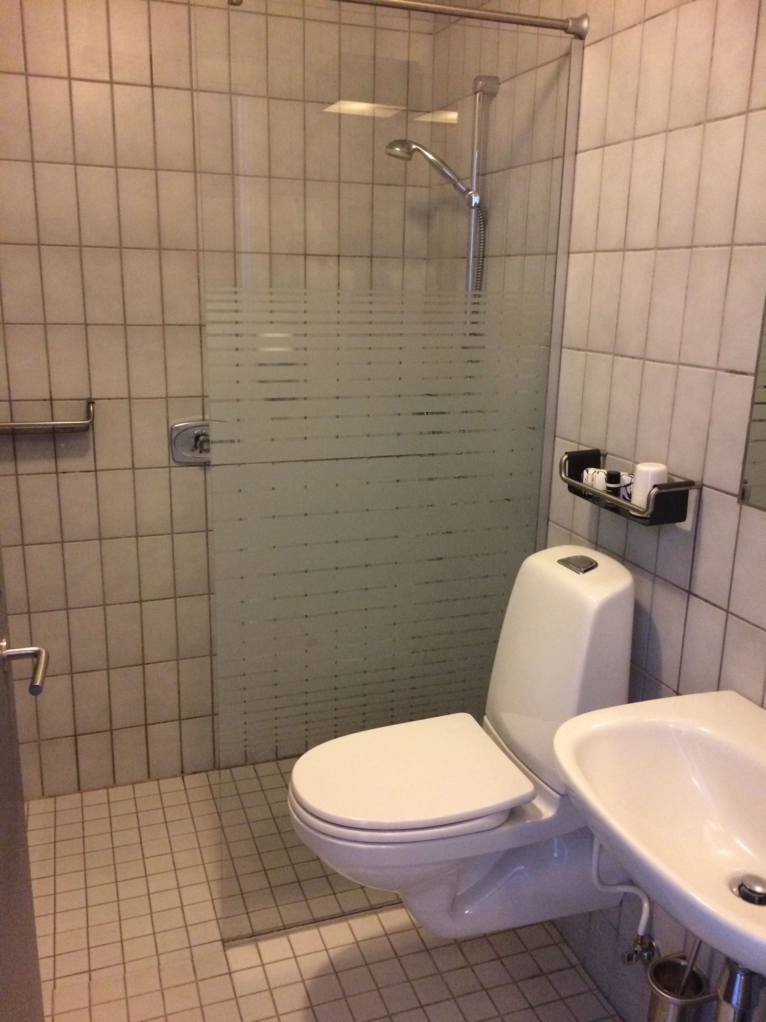 Een kleine betegelde badkamer met toilet, wastafel en douche.