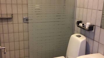 Een kleine betegelde badkamer met toilet, wastafel en douche.