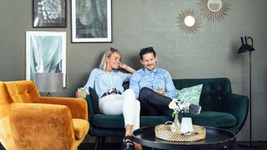 Una sala de estar con un sofá verde, un sillón amarillo y una mesa de centro redonda con un florero y una lámpara.