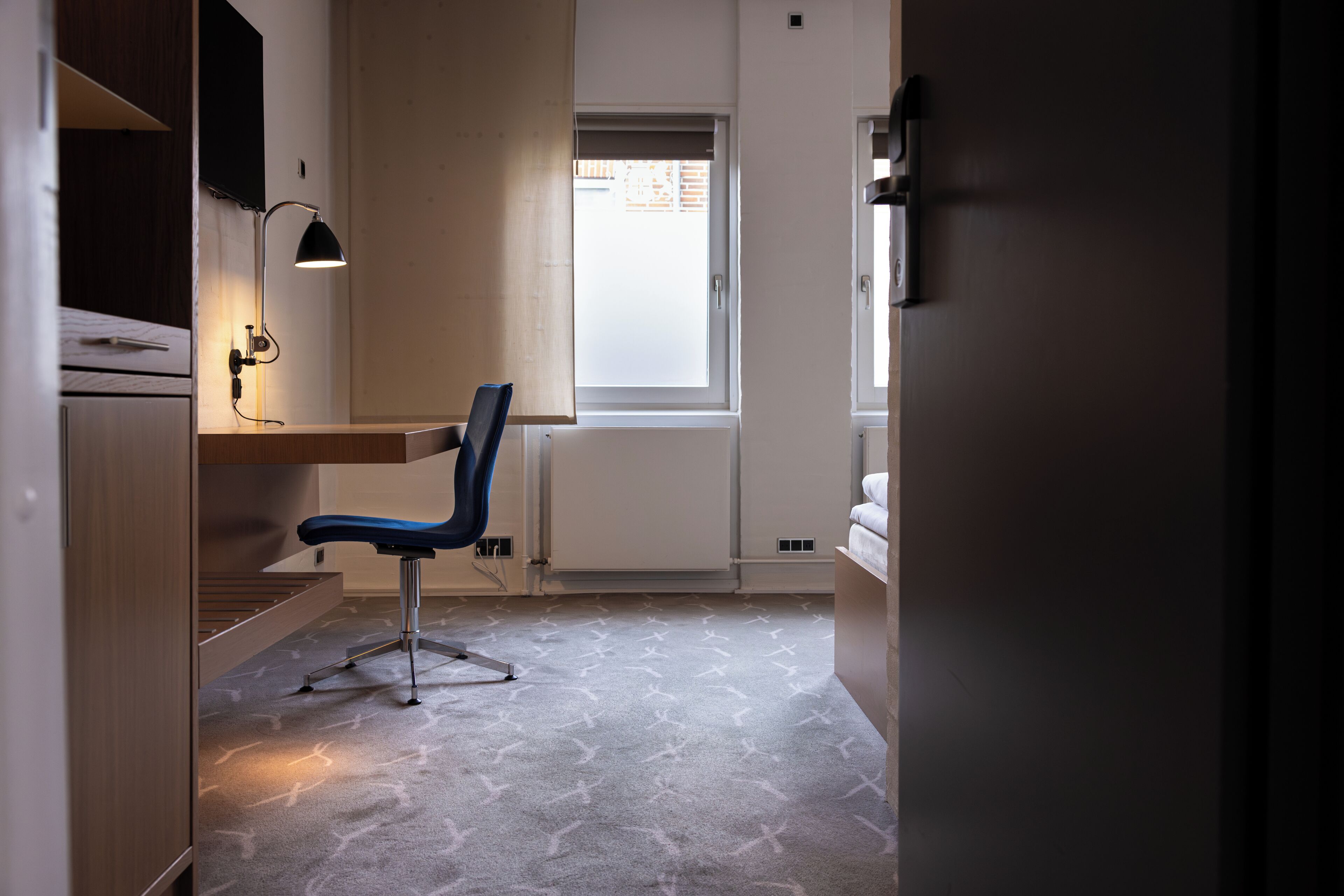 Habitación pequeña con escritorio, silla y ventana.