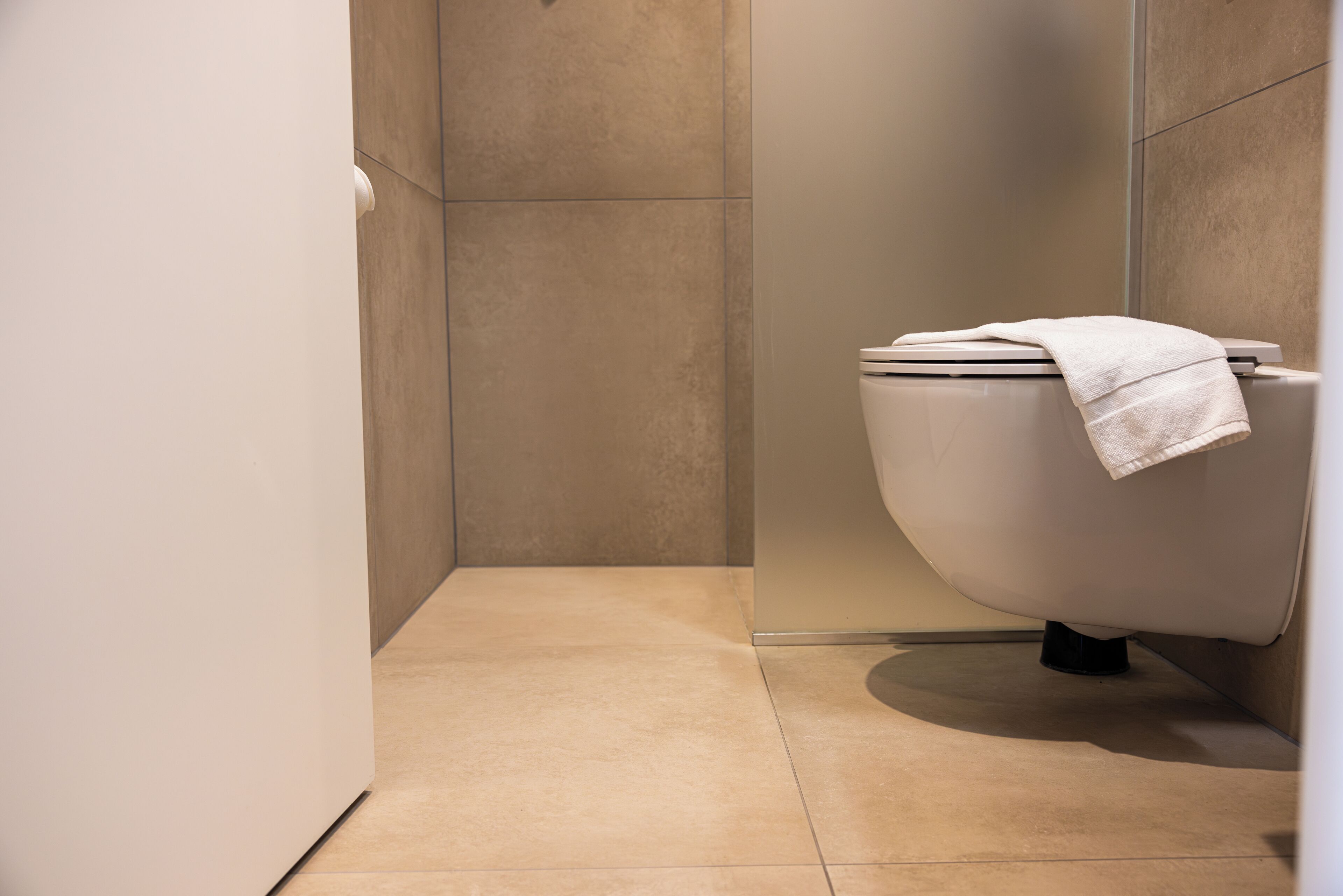 A modern bathroom with a toilet, a towel on the seat, and a tiled floor.
