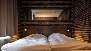 Habitación de hotel con pared de ladrillo, cabecero de madera y una cama grande con ropa blanca.