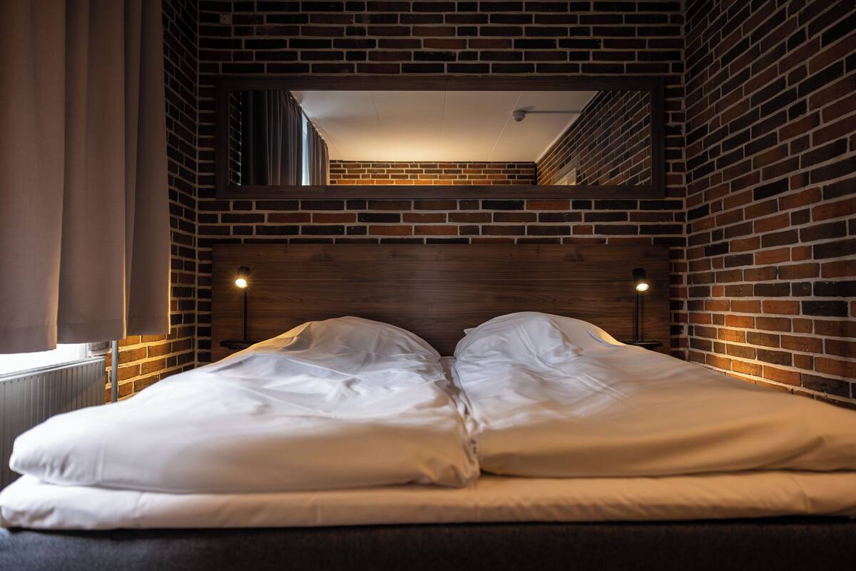 Habitación de hotel con pared de ladrillo, cabecero de madera y una cama grande con ropa blanca.