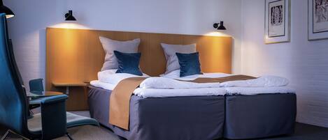 A modern hotel room with a double bed, a desk, and a chair.