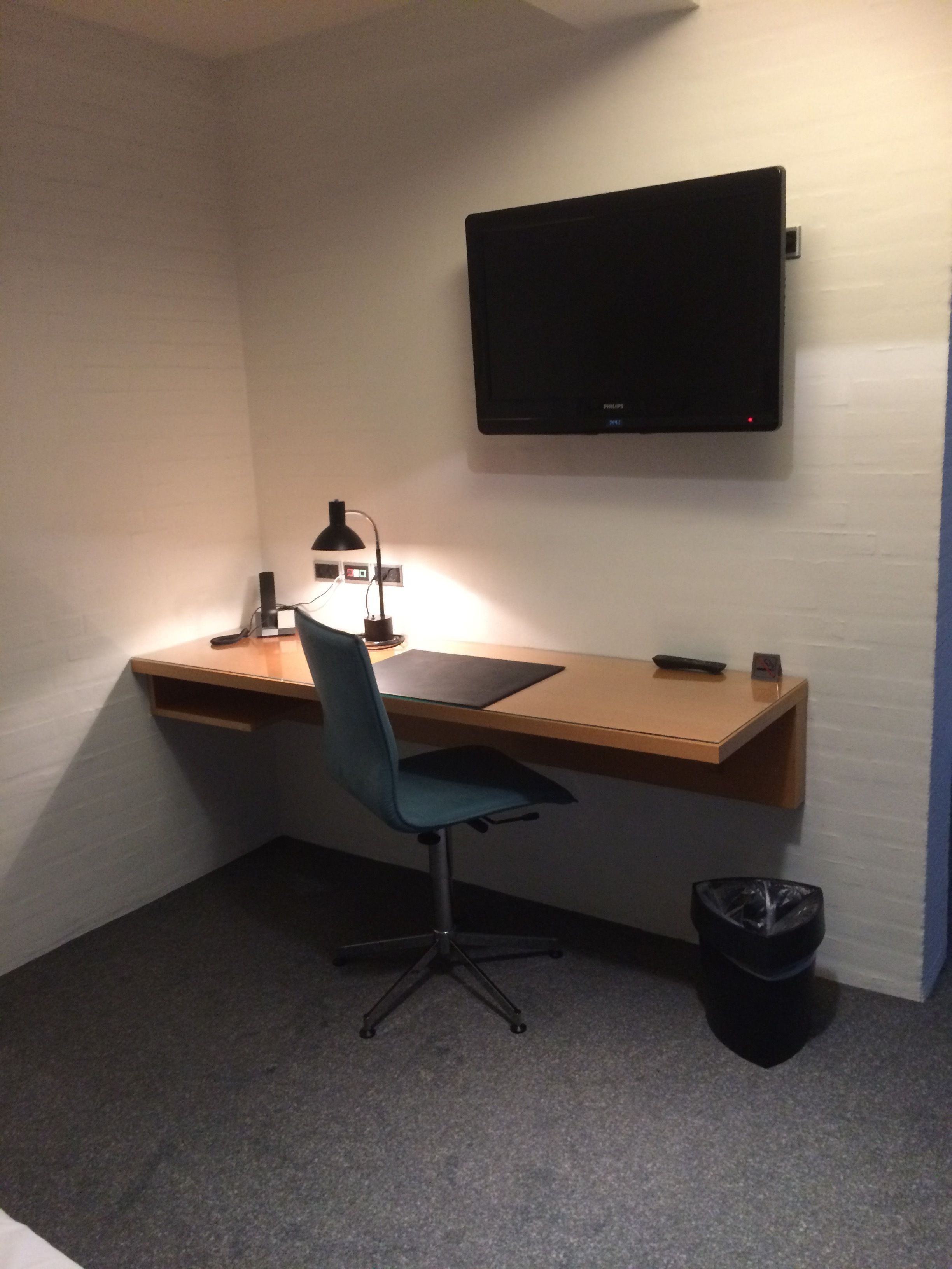 Un espacio de trabajo pequeño y ordenado, con escritorio, silla y televisor montado.