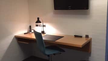 Un espacio de trabajo pequeño y ordenado, con escritorio, silla y televisor montado.