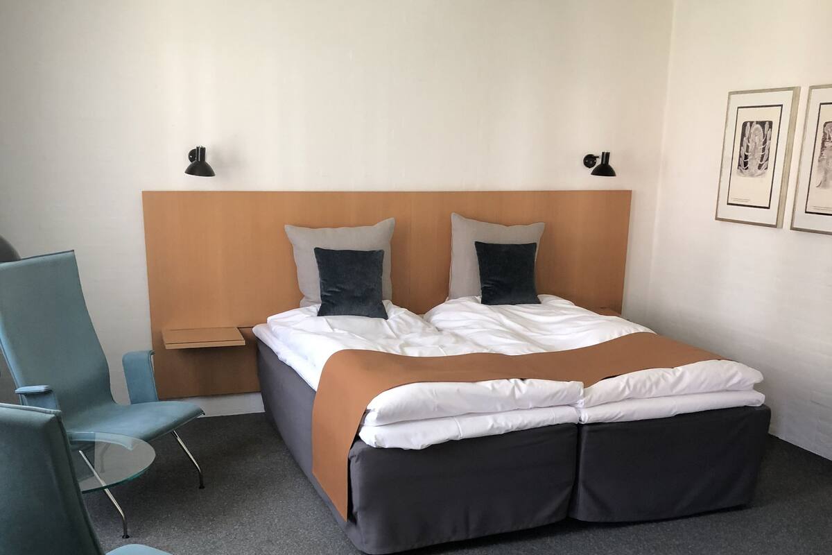 Una habitación de hotel con una cama grande, dos sillones, una mesita y cuadros en la pared.