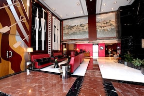 A lobby with a red sofa, a coffee table, and a painting of a coastal scene. - Byblos Hotel Tecom (Dubai)