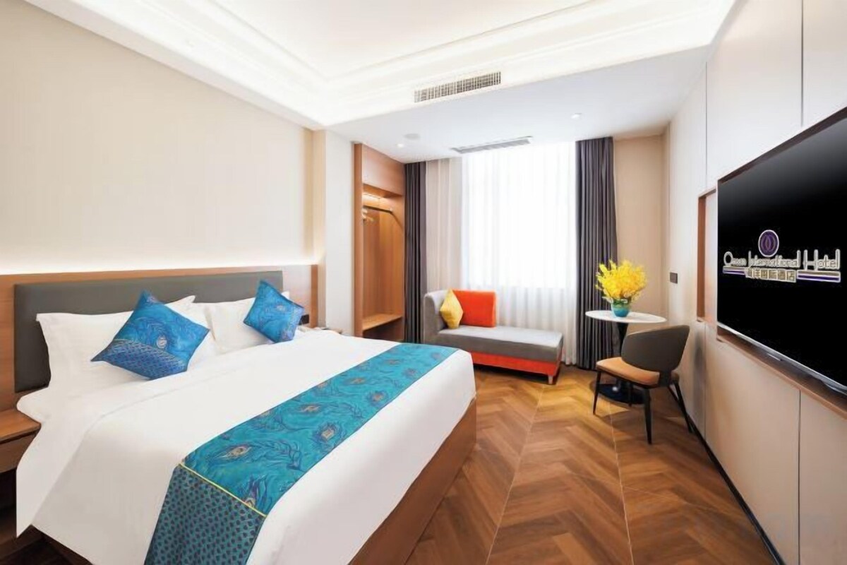 A hotel room with a large bed, a TV, a desk, and a window with curtains.