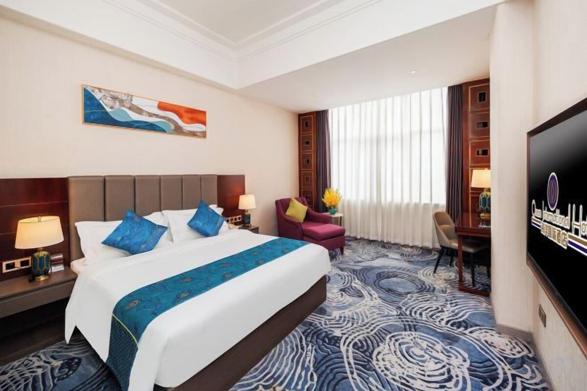 A hotel room with a large bed, a flat-screen TV, a desk, and a chair.