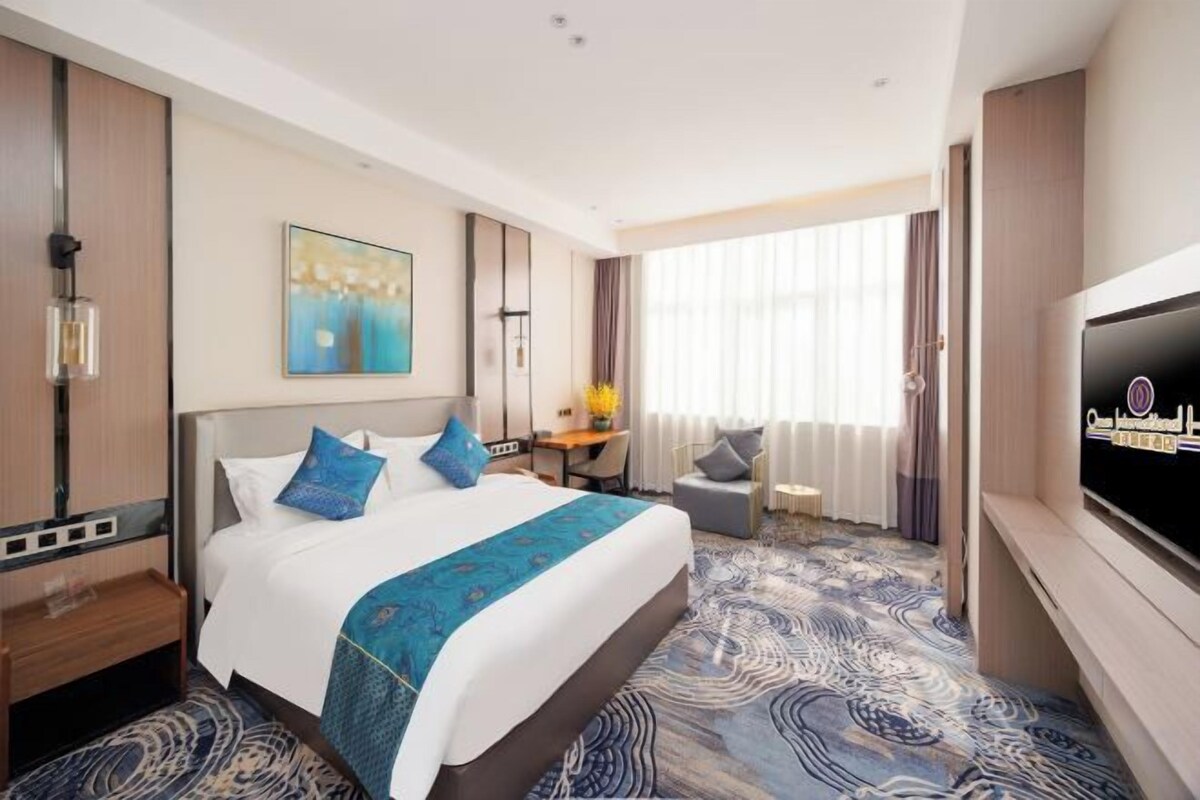 A hotel room with a large bed, a desk, a TV, and a view of the outdoors.