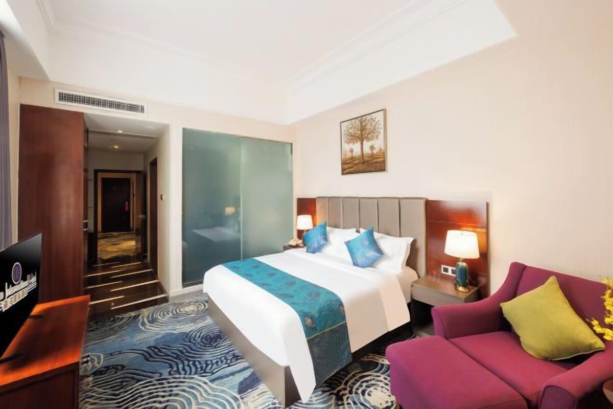 A hotel room with a bed, a desk, a TV, a sofa, and a door leading to another room.