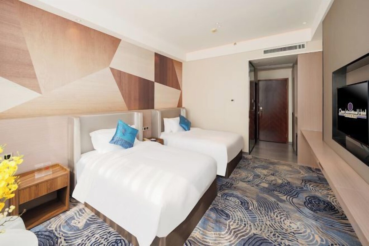 A hotel room with two beds, a TV, and a patterned carpet.