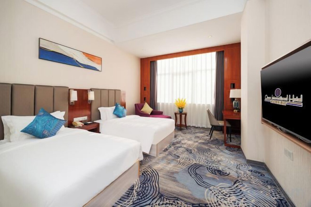 A hotel room with two beds, a television, a desk, and a large window.