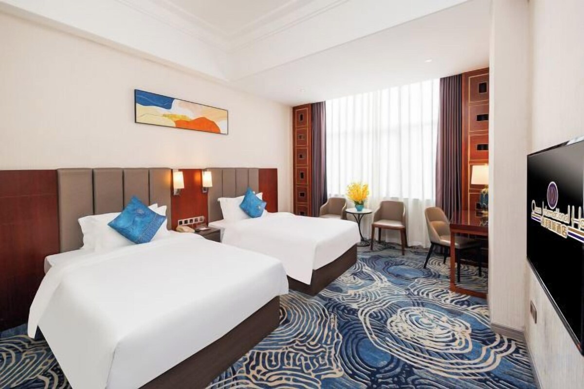 A hotel room with two beds, a TV, a desk with a chair, and a large window.