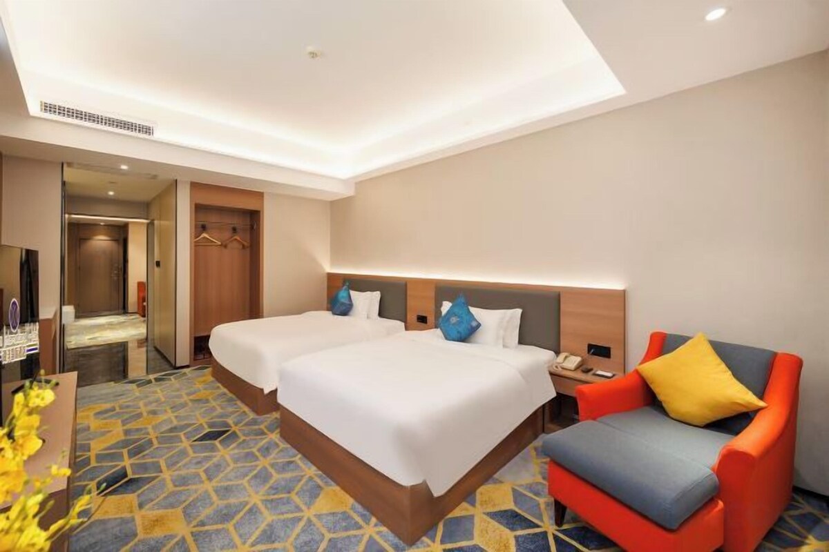 A hotel room with two beds, a sofa, a TV, and a bathroom visible through an open door.