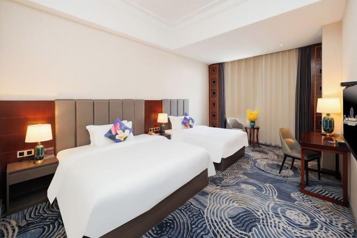 A hotel room with two beds, a desk, a chair, and a television.