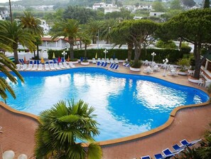 A swimming pool with lounge chairs and umbrellas, surrounded by palm trees and a view of buildings. - Hotel Park Imperial (Forio)