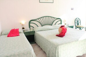A room with two single beds, each with a green metal headboard, a nightstand with a lamp, and a small table with a chair. - Hotel Park Imperial (Forio)
