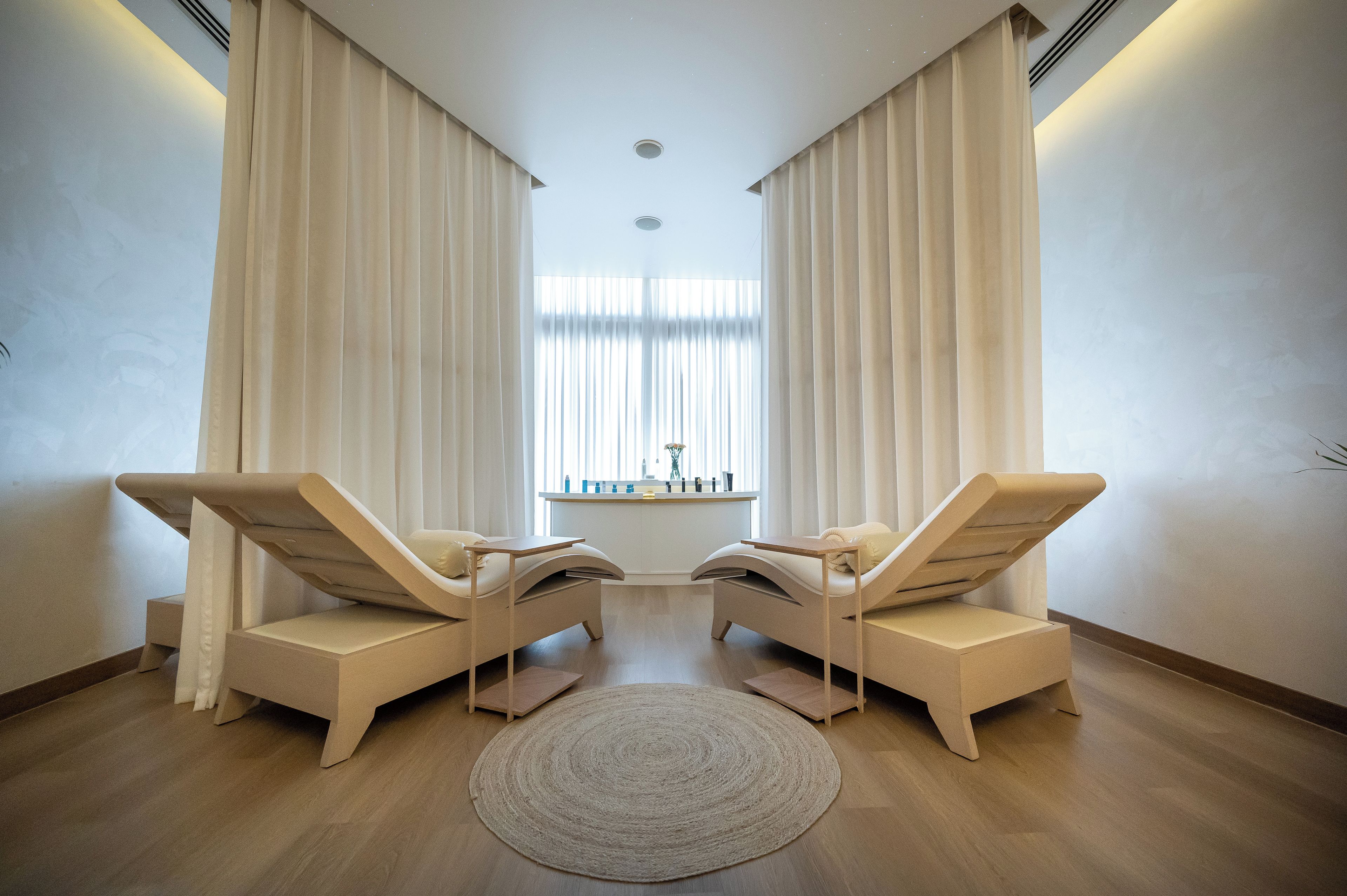 A room with two lounge chairs, a round rug, and a window with curtains.