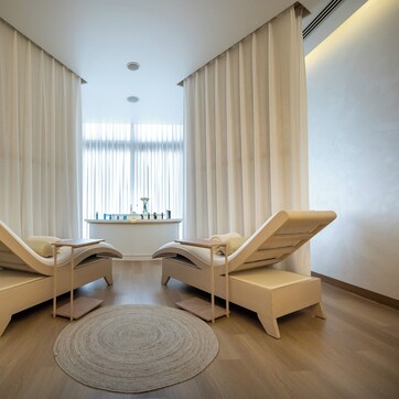 A room with two lounge chairs, a round rug, and a window with curtains.