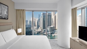 Une chambre d’hôtel avec un grand lit, une télévision, un bureau et une vue sur le paysage urbain grâce à de grandes fenêtres.