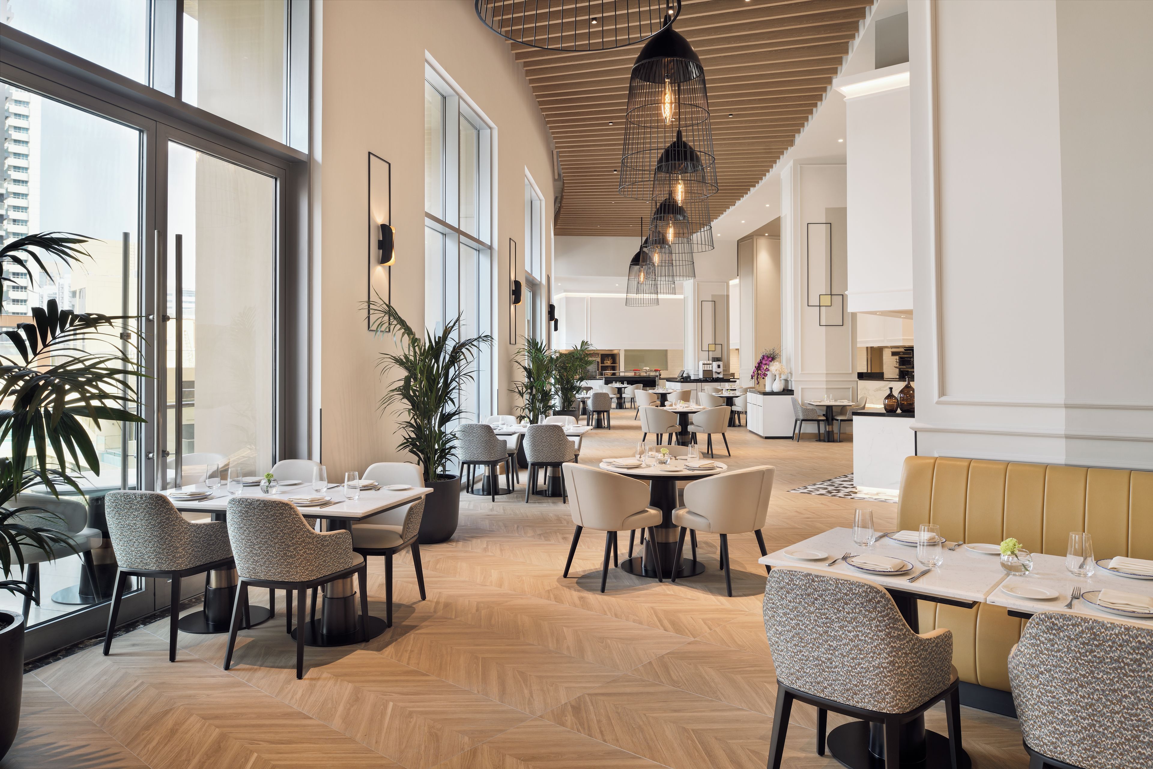 A modern restaurant interior with high ceilings, large windows, and a mix of dining tables and booths.