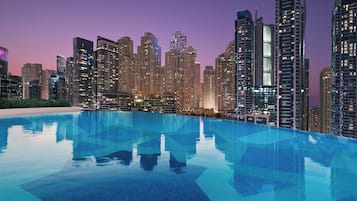 A modern hotel with a rooftop infinity pool overlooking a city skyline at dusk.