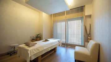 A minimalist room with a bed, a chair, a small table, and a window with blinds.