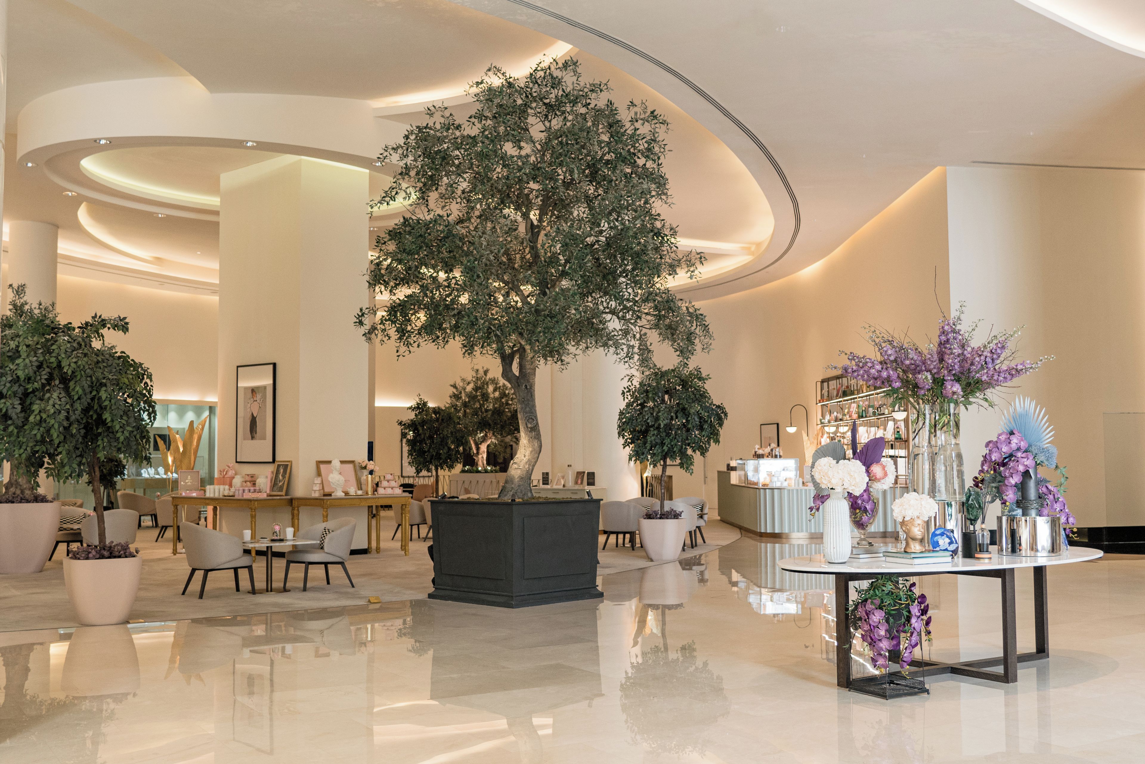 A spacious lobby with a large tree, seating areas, and a reception desk.
