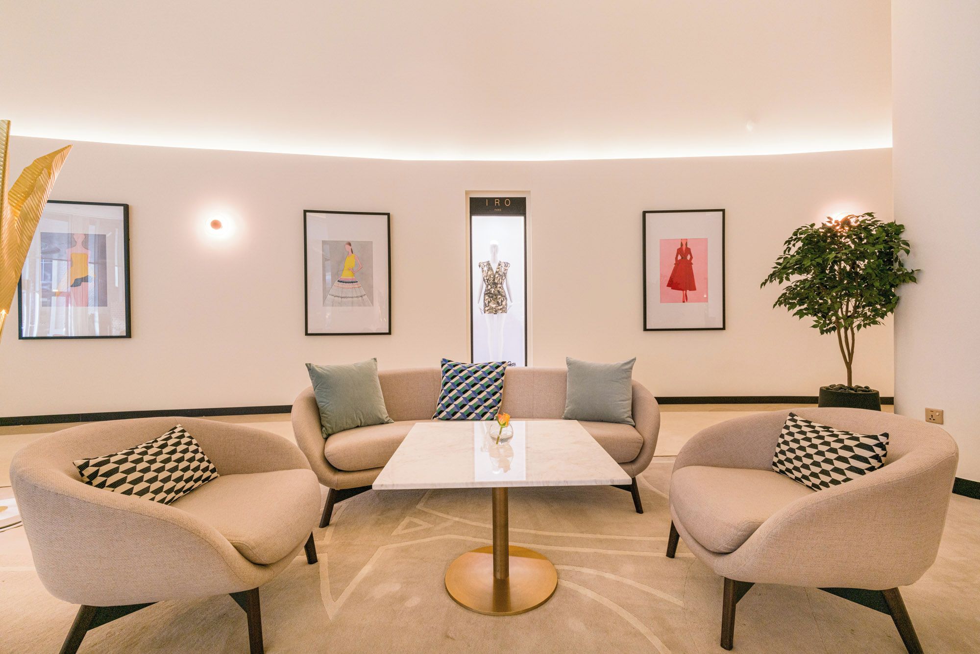 Un espace de détente moderne avec une table ronde, deux fauteuils et un canapé. Des œuvres d’art encadrées ornent les murs, et une plante en pot est placée sur le côté.